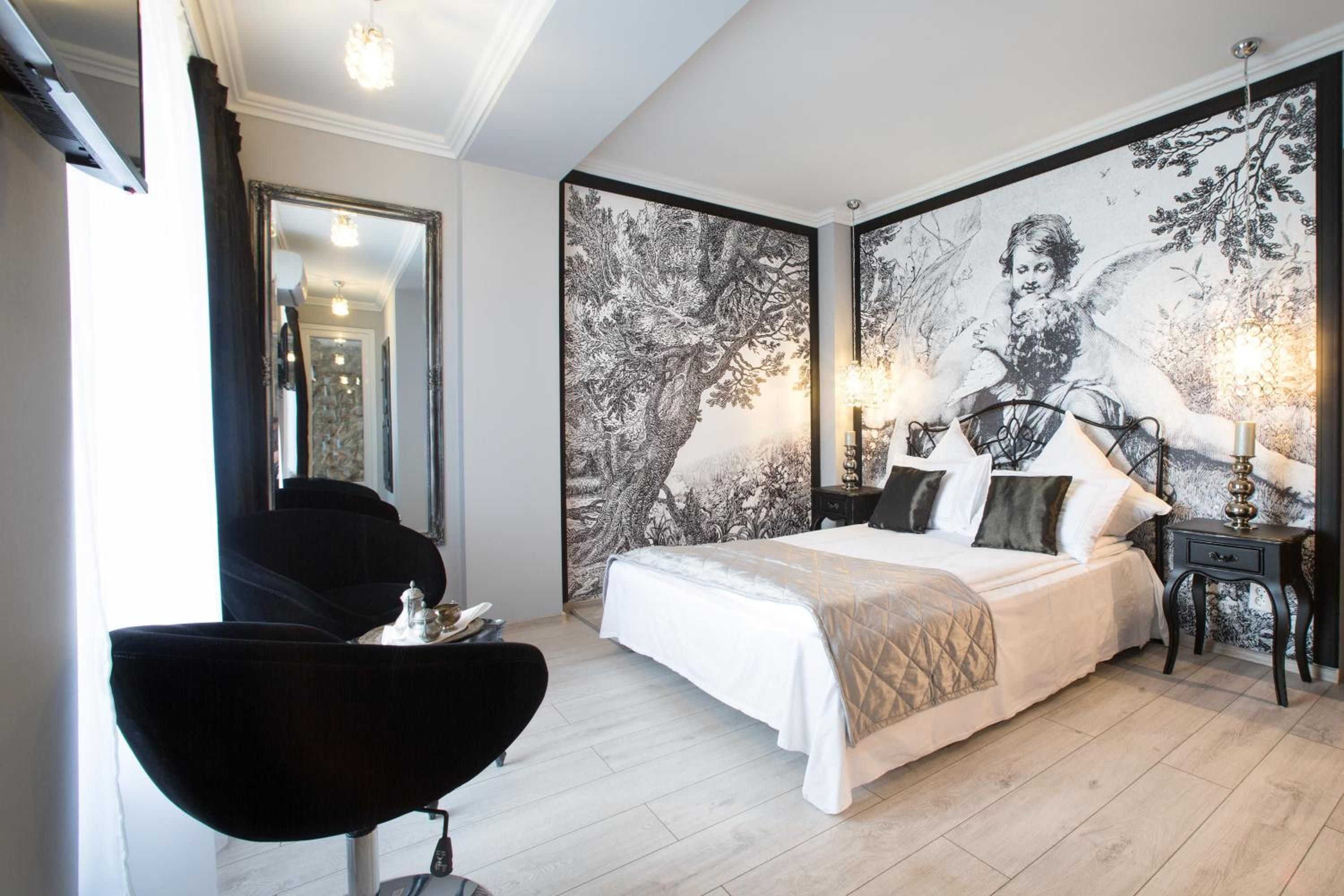A bedroom with a large bed, a chair, a nightstand, and a wall with a detailed mural.