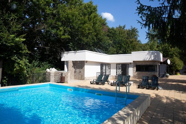 A swimming pool with a modern house in the background, surrounded by trees.