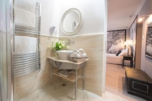 A bathroom with a marble floor, a sink with a vase of flowers, a towel rack, and a mirror.