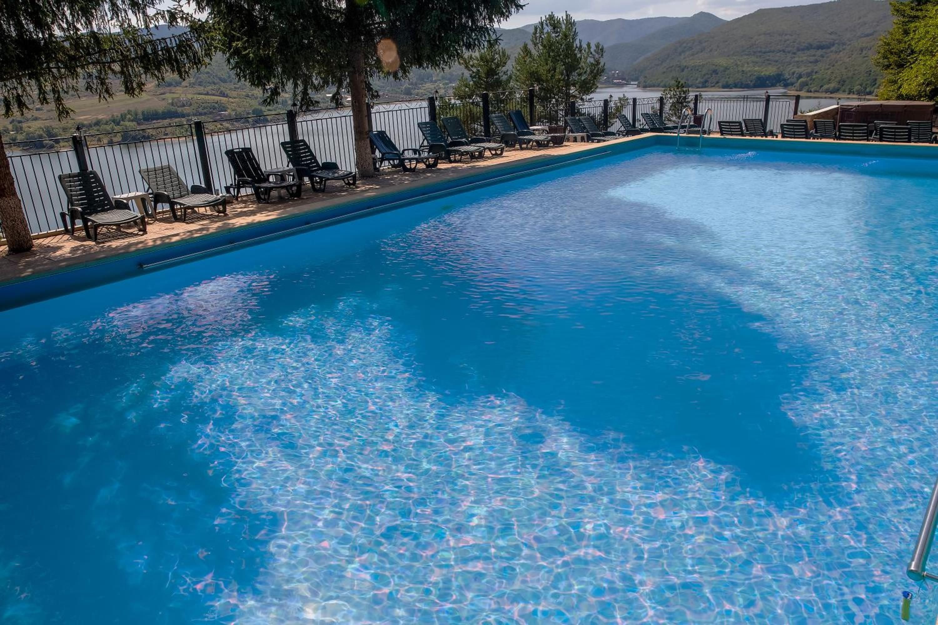 A rectangular swimming pool with clear blue water, surrounded by lounge chairs and a fence.