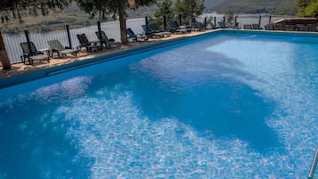 A rectangular swimming pool with clear blue water, surrounded by lounge chairs and a fence.