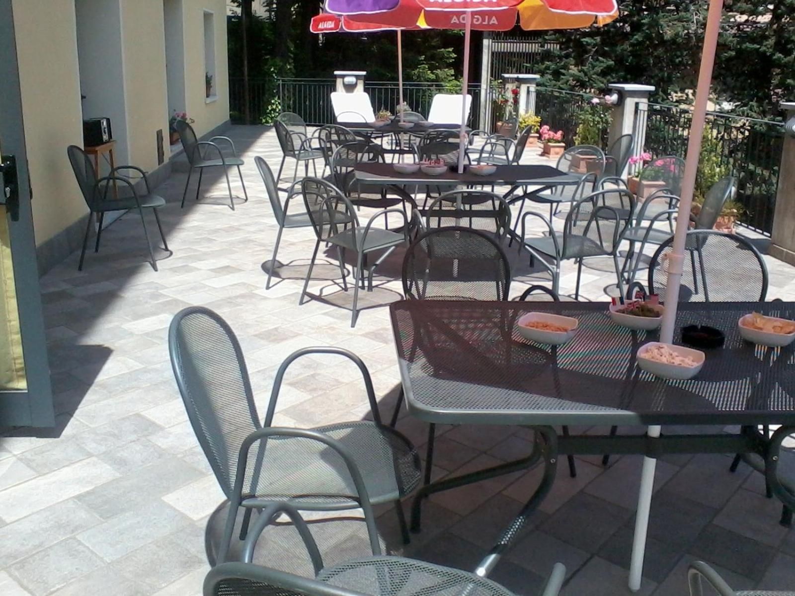An outdoor patio with metal tables and chairs, umbrellas, and a tiled floor.