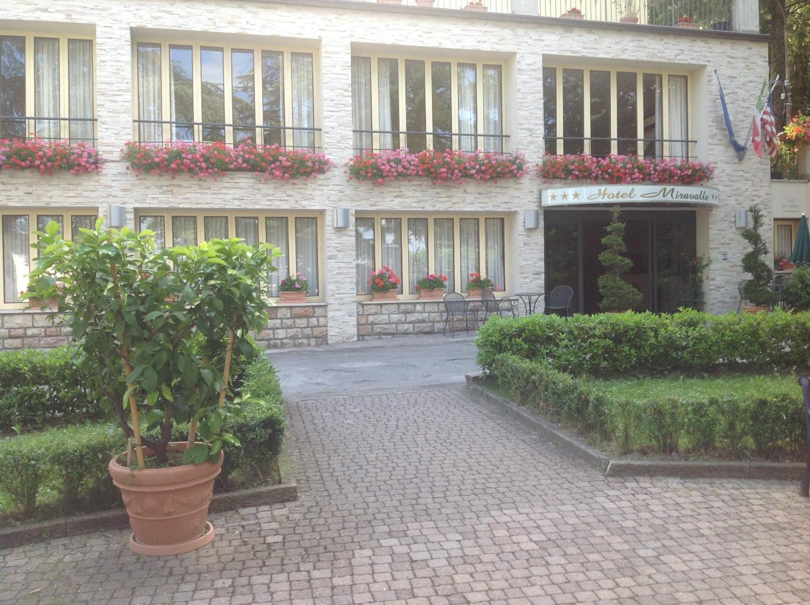 A hotel with a stone facade, multiple windows with curtains, and flower boxes on the balconies.