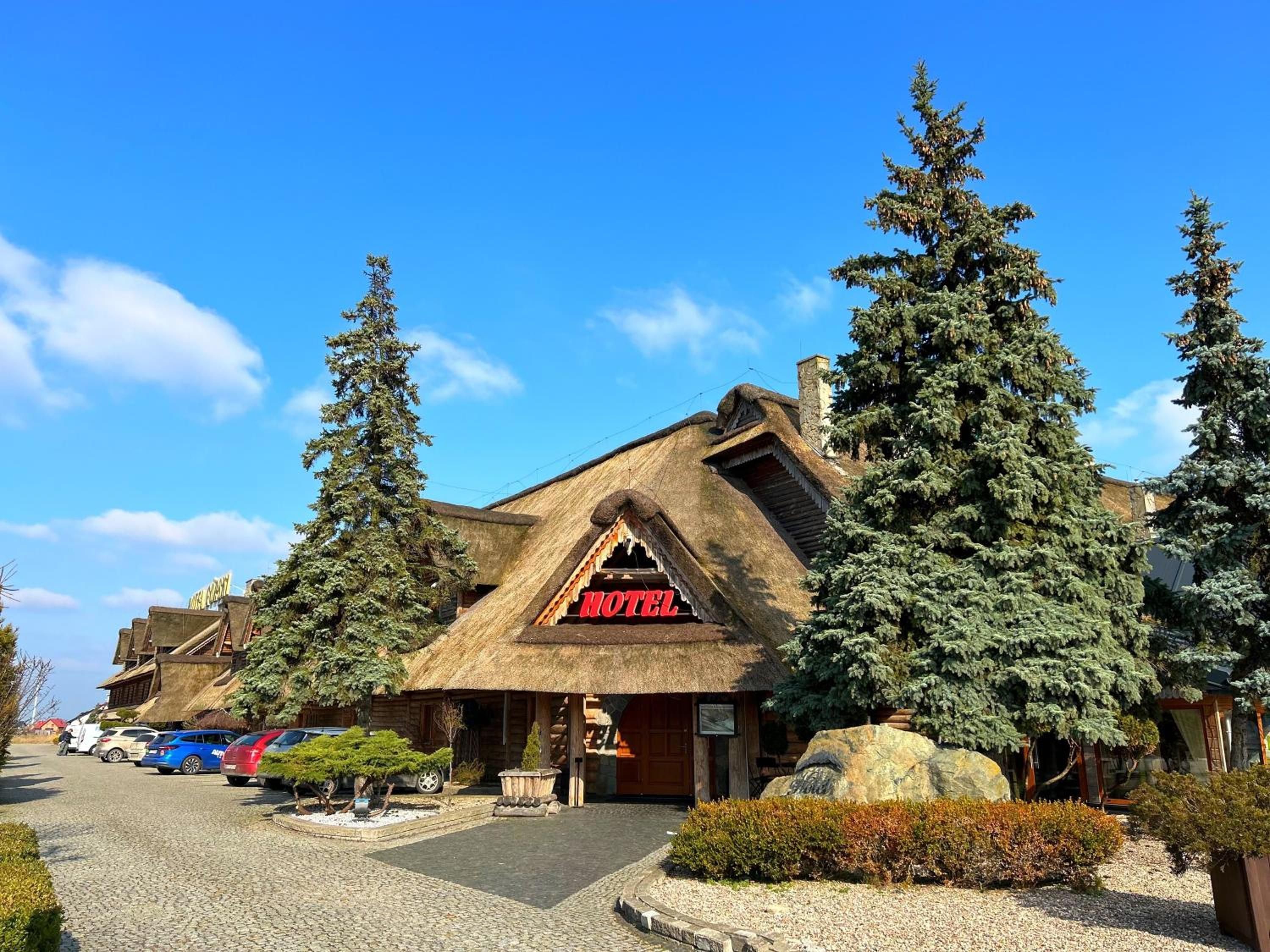 A lodge with a thatched roof, a visible entrance, and a parking area with cars.
