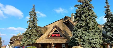 A lodge with a thatched roof, a visible entrance, and a parking area with cars.