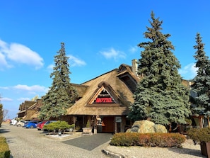 A lodge with a thatched roof, a visible entrance, and a parking area with cars.