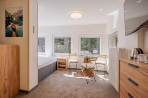 Un dormitorio moderno con una cama, un escritorio pequeño, una silla, un radiador y una ventana.