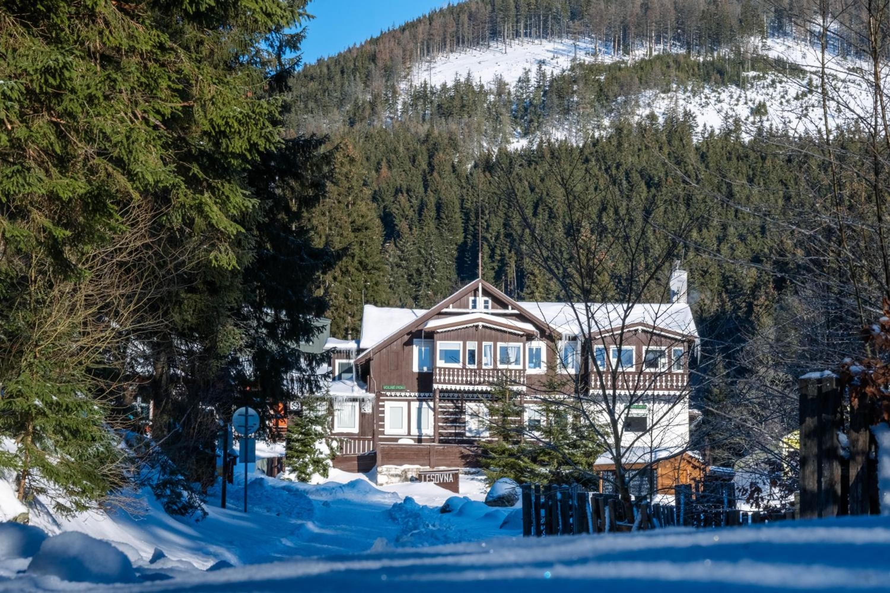 A two-story wooden building with a balcony, surrounded by snow and trees.