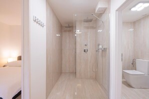 Un baño moderno con ducha, inodoro y una cama en la habitación contigua.