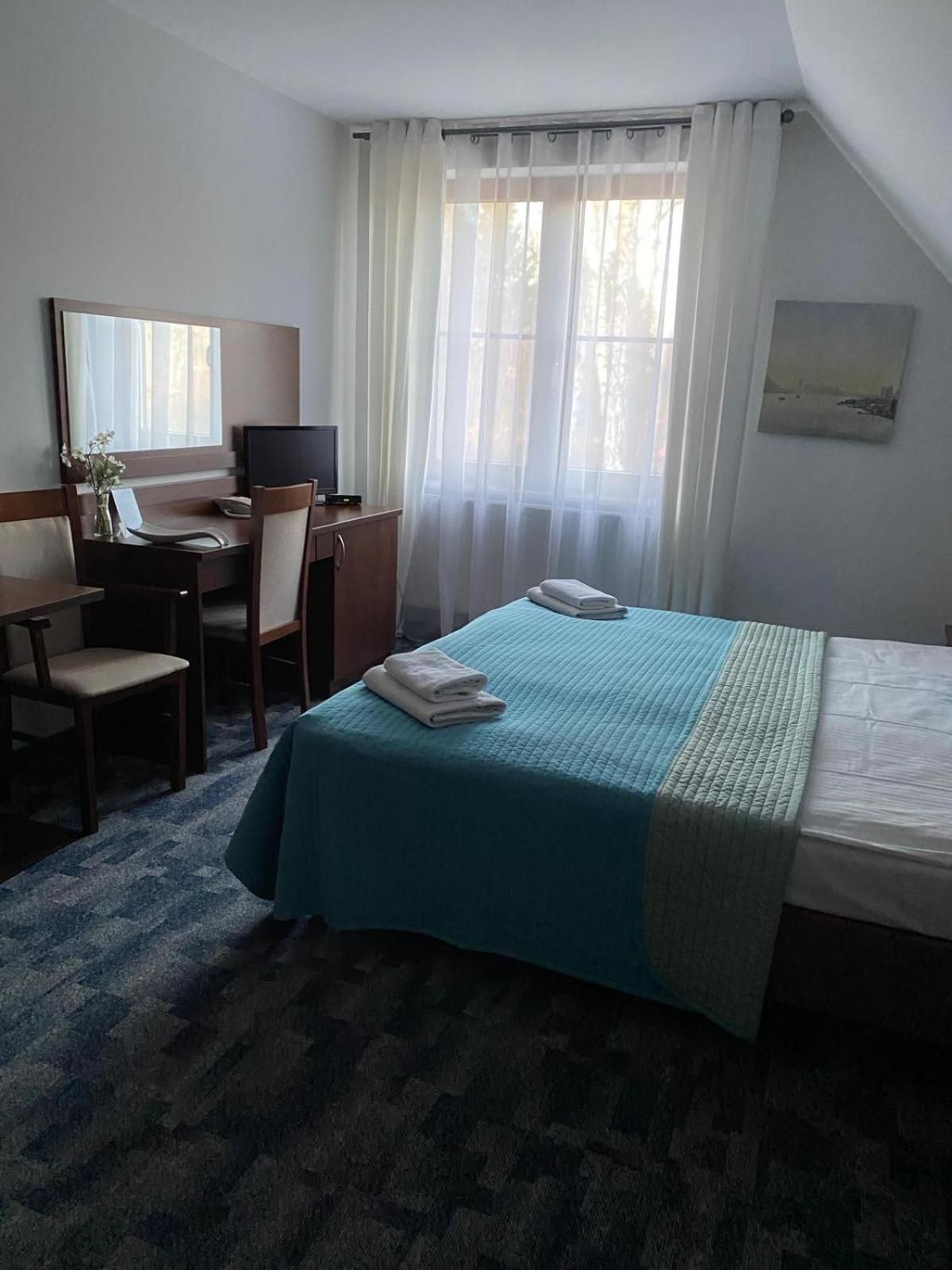 Una habitación de hotel con una cama, un escritorio con una silla, un televisor y una ventana con cortinas.