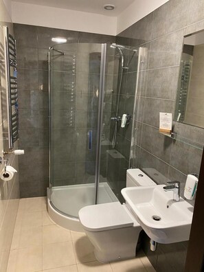 Casa de banho moderna com chuveiro envolto em vidro, sanita e lavatório.