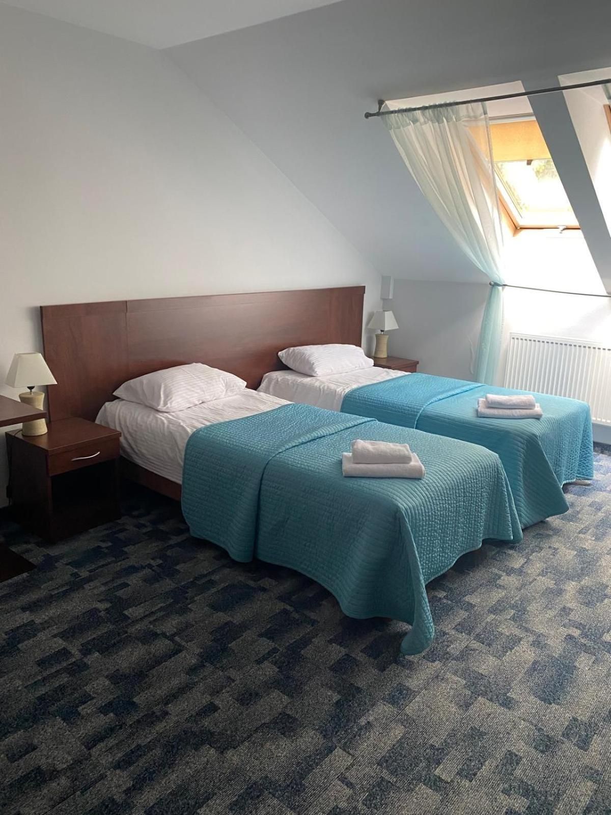 Habitación de hotel con dos camas, una mesita de noche, una lámpara y una ventana con cortinas.