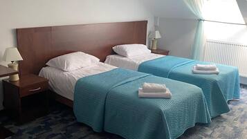 Habitación de hotel con dos camas, una mesita de noche, una lámpara y una ventana con cortinas.
