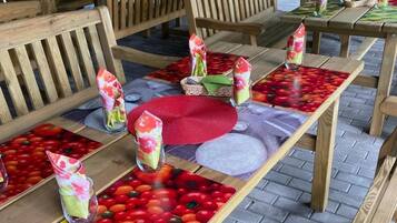 Outdoor wooden tables with benches, arranged in a garden setting.
