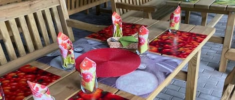 Outdoor wooden tables with benches, arranged in a garden setting.