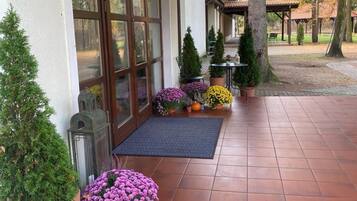 Un espacio al aire libre techado con piso de baldosas, plantas en macetas y una pérgola de madera.
