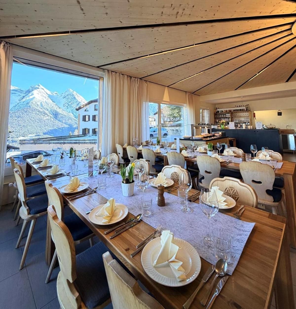 A dining area with tables set for a meal, chairs, and a view of mountains through large windows.