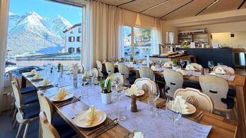 A dining area with tables set for a meal, chairs, and a view of mountains through large windows.