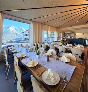 A dining area with tables set for a meal, chairs, and a view of mountains through large windows. - Hotel Bellavista Ftan (Scuol)