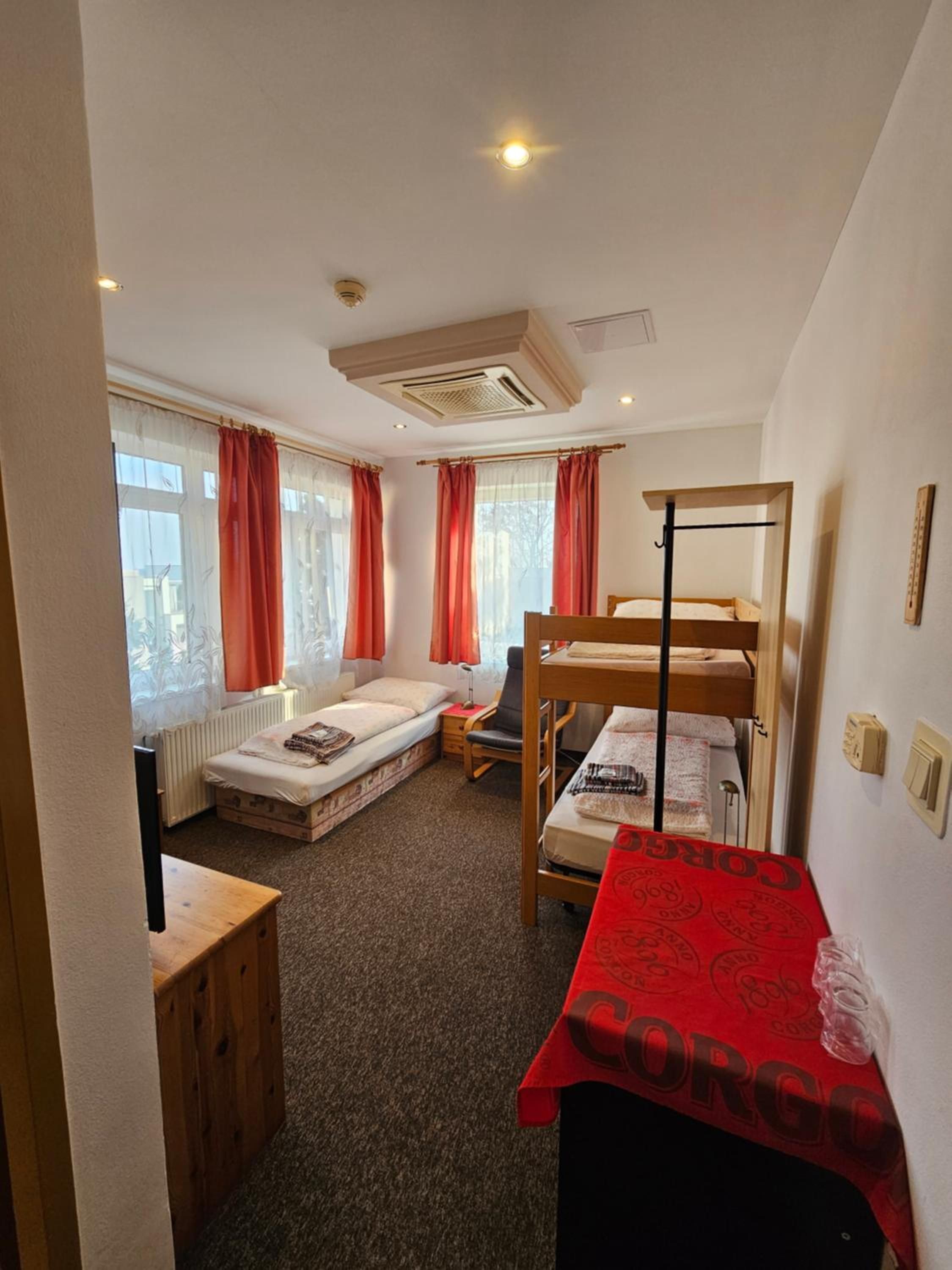 Ein Schlafsaalzimmer mit Etagenbetten, einem kleinen Schreibtisch, einem Heizkörper und einem Fenster mit Vorhängen.