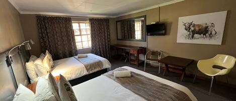 A hotel room with two beds, a desk, a chair, a television, and a painting on the wall.