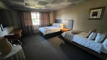 Une chambre d’hôtel avec deux lits, un bureau, une chaise, une fenêtre avec des rideaux et un tableau encadré au mur.