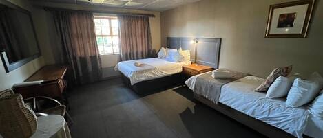 A hotel room with two beds, a desk, a chair, a window with curtains, and a framed picture on the wall.