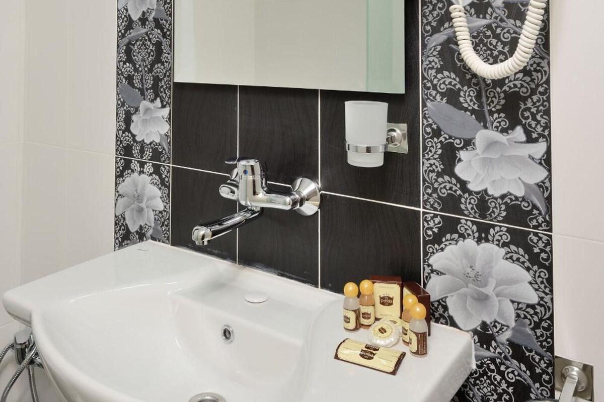 Un baño con lavamanos blanco, espejo, secador de pelo y artículos de aseo.