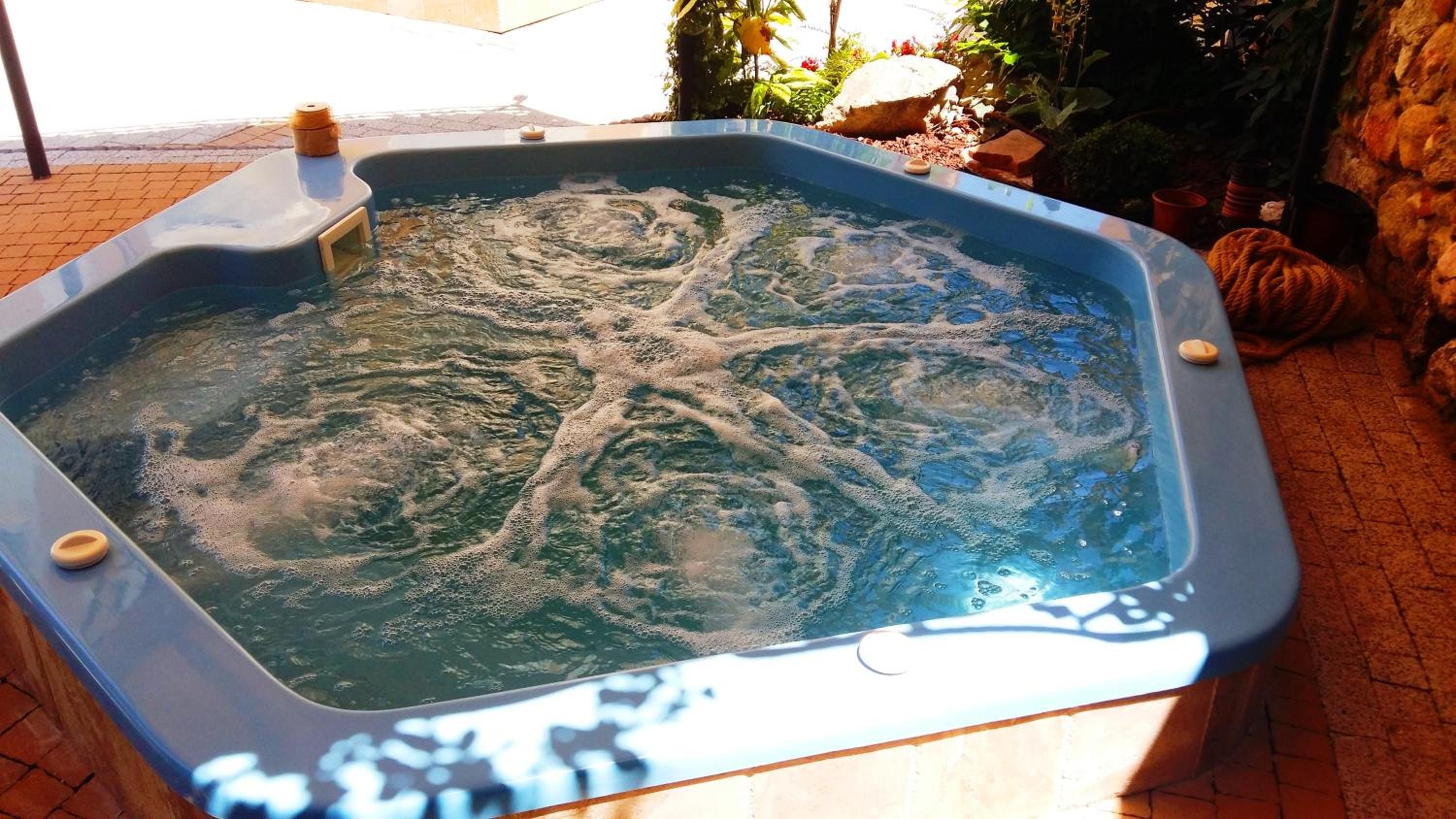 A hot tub with a stone wall and plants in the background.