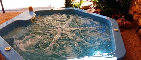 A hot tub with a stone wall and plants in the background.