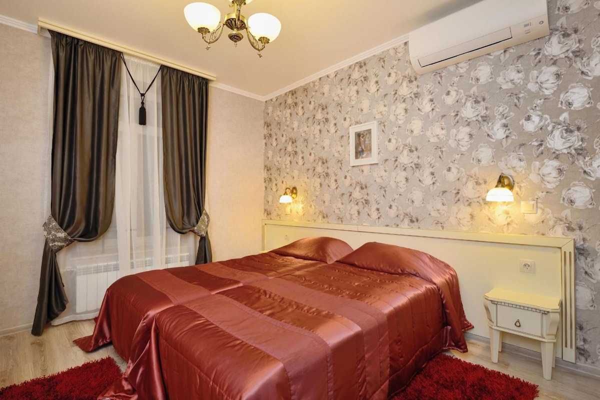 Habitación de hotel con cama, mesita de noche, lámpara, aire acondicionado y ventana con cortinas.