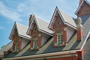 A building with a steeply pitched roof, brick construction, and multiple chimneys. - De Statie (Brecht)