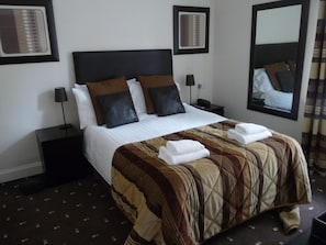 Habitación de hotel con cama, mesita de noche, lámpara, espejo y aire acondicionado instalado en la pared.