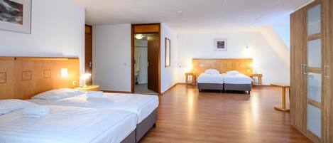 Quarto de hotel com duas camas, piso de madeira e banheiro visível através de uma porta aberta.