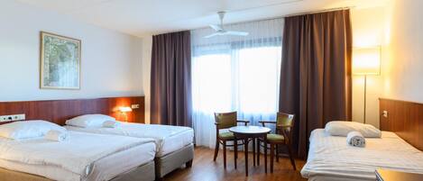Habitación de hotel con dos camas, un escritorio, una silla, una mesa, un ventilador de techo y una ventana con cortinas.