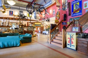 Um quarto com uma escada, um sofá e diversos objetos expostos, incluindo bicicletas e uma máquina de escrever.