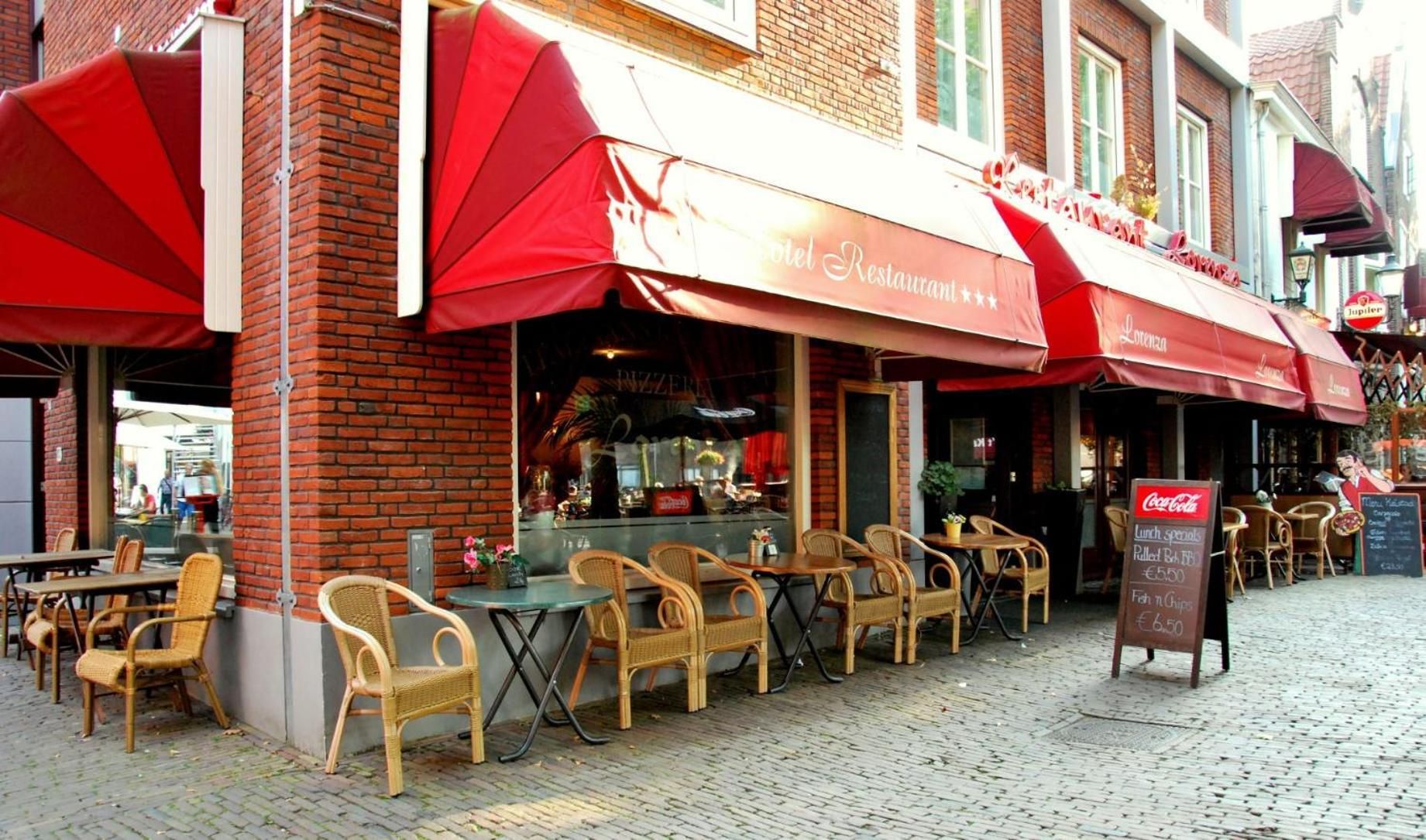 A brick building with outdoor seating and red awnings, featuring a sign for a restaurant and a Coca-Cola sign.