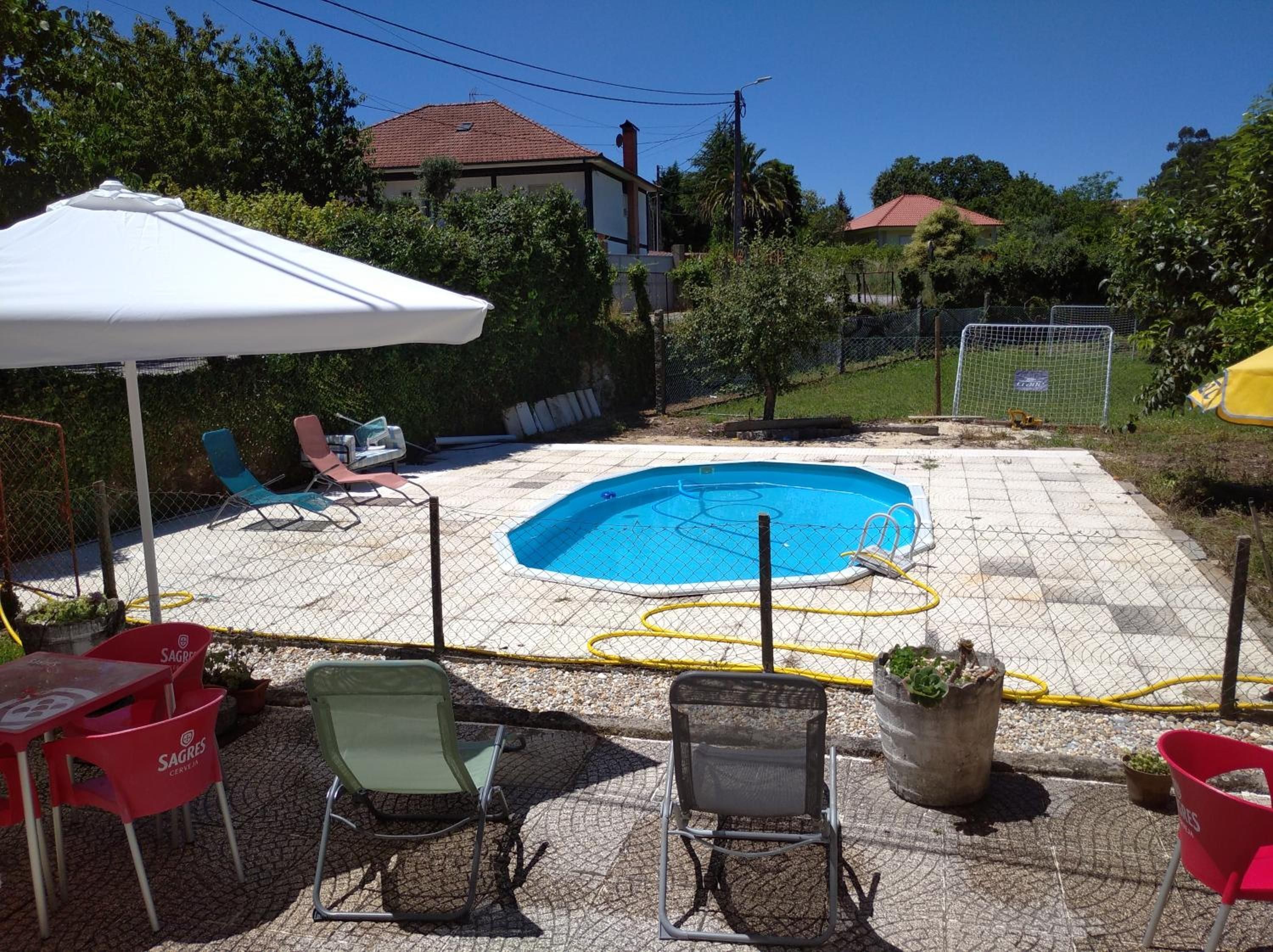 Un patio trasero con piscina, sillas de exterior y una mesa.
