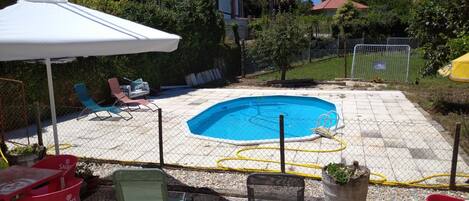 Un patio trasero con piscina, sillas de exterior y una mesa.