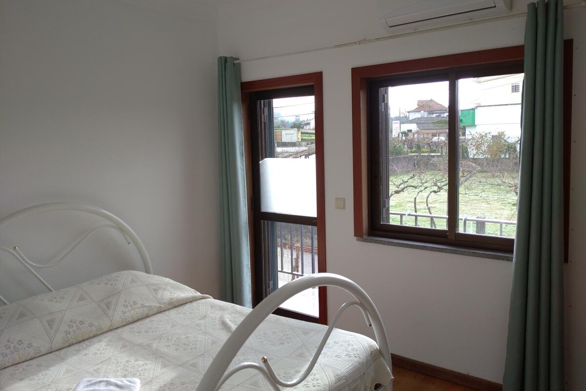 A room with a bed, a window with a view of a garden, and an air conditioning unit.