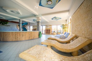 Espaço de spa com balcão de recepção, cadeiras de descanso e uma grande janela.