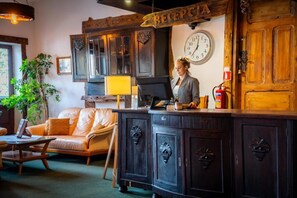 Uma área de recepção com uma mesa de madeira, um relógio e uma placa com a inscrição 'RECEPCIA'.