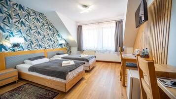 A hotel room with two beds, a desk, a TV, and a window with curtains.