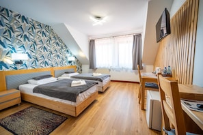 Ett hotellrum med två sängar, ett skrivbord, en TV och ett fönster med gardiner.