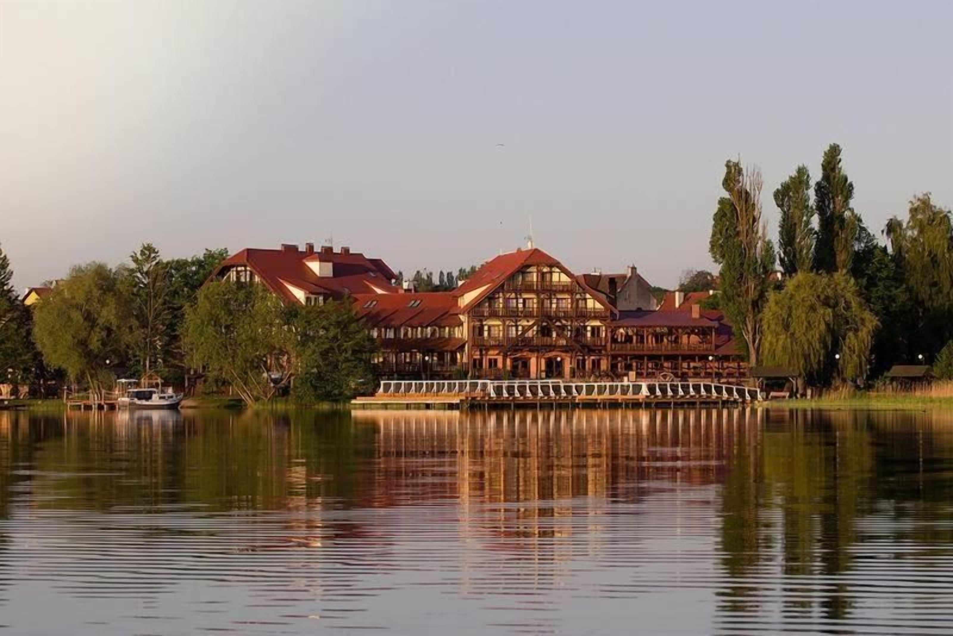 A lakeside hotel with a large building, a dock, and trees.