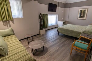 Una habitación con una cama, una silla, una mesita y un ventanal con cortinas.
