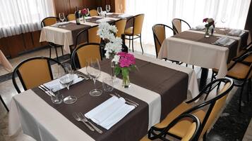 A restaurant with tables set for dining, featuring white and brown tablecloths, chairs, and floral centerpieces.
