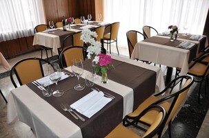 Un restaurante con mesas dispuestas para comer, con manteles blancos y marrones, sillas y centros de mesa con flores.