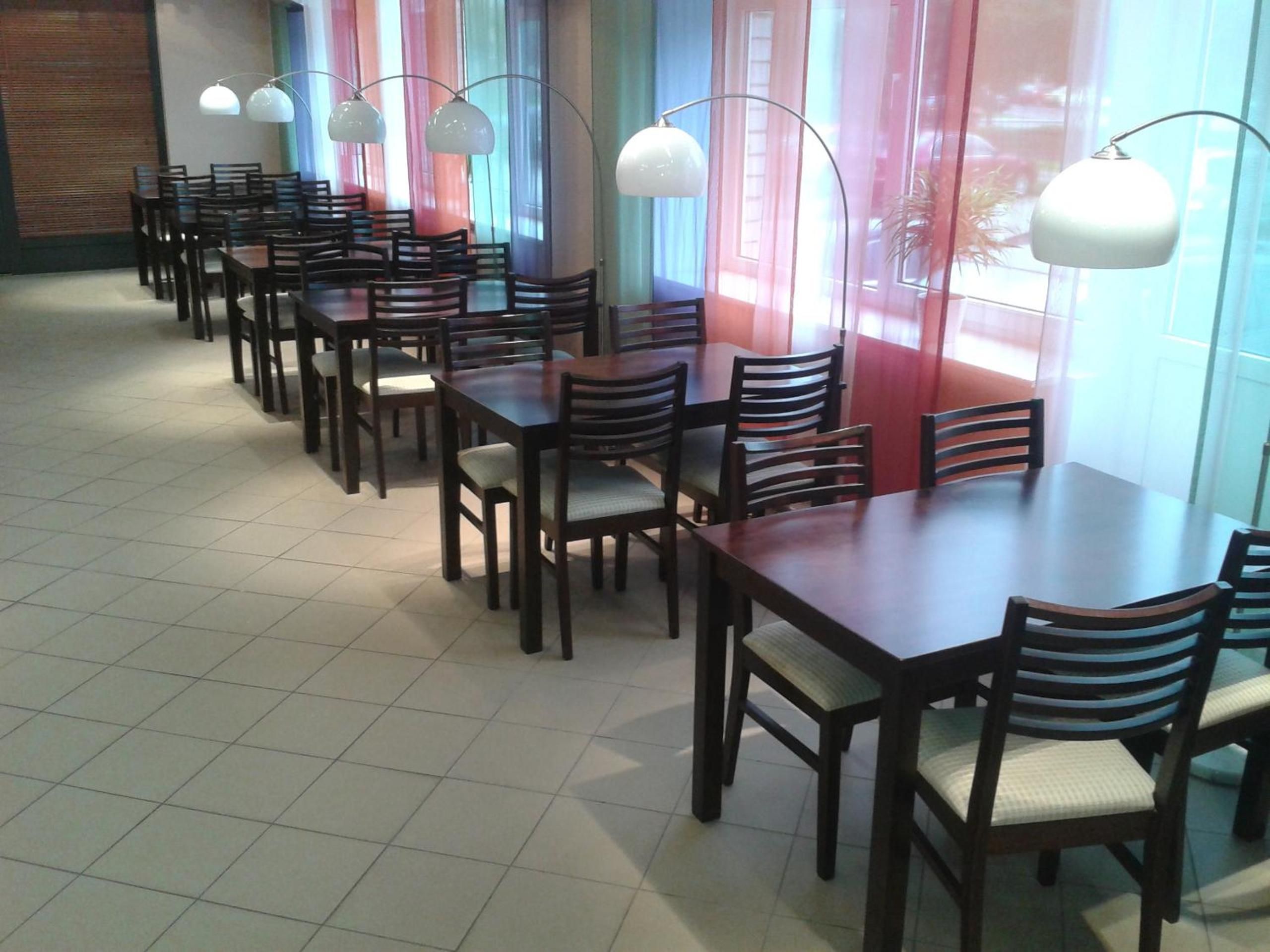 A dining area with multiple tables and chairs, large windows with curtains, and pendant lighting.