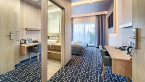 Ein Hotelzimmer mit Schreibtisch, Stuhl, Bett und einem durchgehenden Türspalte sichtbaren Badezimmer.